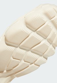 Sole of a shoe in a textured cream color, featuring raised geometric patterns and grooves for traction and grip. Durable rubber material.