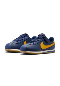 Baskets Nike en cuir bleu marine avec des accents jaunes. Elles possèdent un design à lacets, une semelle en caoutchouc texturée et des détails cousus.