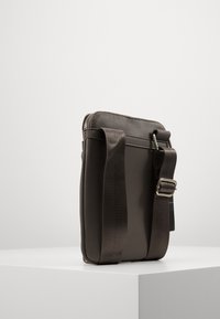 Dark brown crossbody bag with a textured exterior, zip closure, adjustable strap, and metal hardware. Compact rectangular shape.