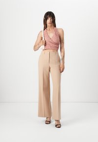Pink patterned halter crop top with a ruching detail, paired with high-waisted beige wide-leg trousers and black heeled sandals.