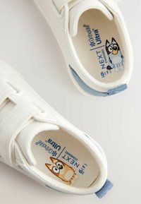Witte sneakers met klittenbandsluitingen, met lichtblauwe accenten. Het interieur heeft een cartoonpersonage ontwerp en "Ortholite" branding.