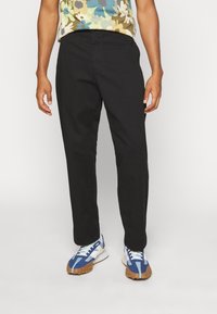 Czarna, prosta para spodni o gładkiej teksturze, w połączeniu z wzorzystą, wielokolorową bluzką oraz niebieskimi butami sportowymi z białymi akcentami.