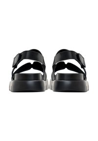Paar schwarze Plateausandalen mit verstellbaren Knöchelriemen, von hinten auf weißem Hintergrund gesehen.