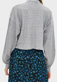 Pull court gris côtelé avec manches ballon longues, porté sur une jupe noire à motifs floraux bleus. Design simple et fonctionnel.