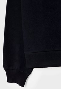 Pull en maille noir à manches longues avec poignets et ourlet côtelés sur un fond clair.