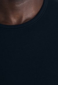 Schwarzes Rundhals-T-Shirt aus Baumwolle. Der Stoff ist glatt mit einem leichten Glanz, hat einen schlichten, einfachen Halsausschnitt und keine sichtbaren Muster.