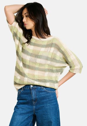 Strickpullover im hellgrünen und beigen Karomuster, mit lockerer Passform, kurzen Ärmeln und atmungsaktivem Material. Kombiniert mit blauen Jeans.