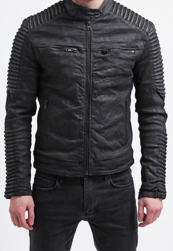 Homme portant une veste en cuir noire cintrée avec des détails côtelés aux épaules et aux manches, associée à un pantalon noir.