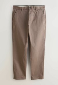 Ruskeat suoralahkeiset housut vyölenkeillä, sivutaskuilla ja nappisuljennalla yksinkertaisella vaalealla taustalla.