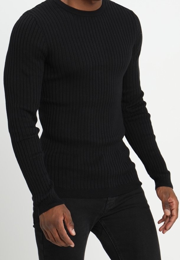 Homme portant un pull noir côtelé ajusté à manches longues et un pantalon noir, montré du cou aux hanches sur fond blanc.