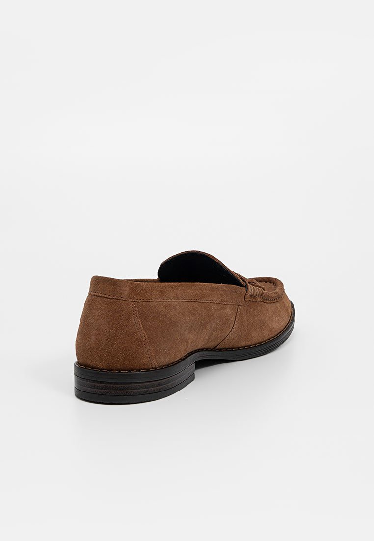 Braune Wildleder Slipper mit abgerundetem Zehenbereich, sichtbarem Nähedetail an der Vorderseite und einer schwarzen Gummisohle. Glatte Textur mit einem lässigen Design.