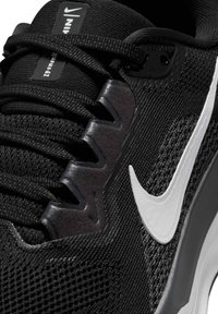 Czarne sneakersy Nike z teksturowaną siateczką, białym logo, wzmocnionymi oczkami i kontrastującymi ciemnymi akcentami na szarej podeszwie.