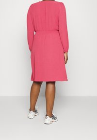 Rosa klänning med lång puffärm, elastisk midja och knälång design. Matchad med vita och grå sportskor.