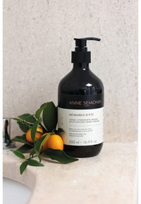 Black glass pump bottle of hand cream with white label, 500 ml. Surrounded by green leaves and kumquats on a light stone surface.