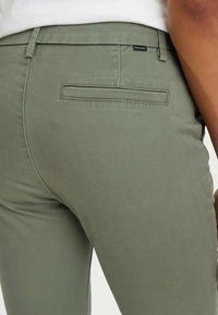 Olivgröna skräddarsydda byxor i slätt tyg, med en bakficka med en diskret söm och en märkesetikett vid midjan.