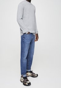 Gray ribbed long-sleeve sweater, relaxed fit, paired with light blue straight-leg jeans and multi-color athletic shoes with dark accents.