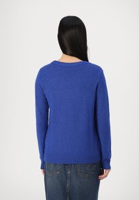 Pull en tricot bleu avec manches longues et encolure arrondie. Ourlet côtelé à la taille et aux poignets ; texture lisse.