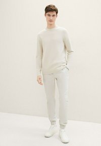 Suéter claro y texturizado de manga larga combinado con pantalones ajustados claros y zapatillas blancas, con puños elásticos en los tobillos.