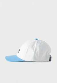 Λευκό καπέλο μπέιζμπολ με ανοιχτό μπλε γείσο και κουμπί, λογότυπο Patagonia στο μπροστινό μέρος και ρυθμιζόμενο λουράκι στο πλάι, πάνω σε λευκό φόντο.