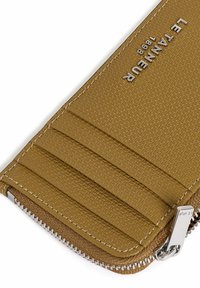 Billetera de cuero marrón texturizado con logo grabado, cierre de cremallera y ranuras para tarjetas en un lado. Los detalles en acero inoxidable realzan el diseño.