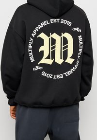 Sudadera negra de mezcla de algodón, con un gran gráfico blanco que lleva impreso "M" y "MULTIPLY APPAREL EST 2015" en la parte posterior.