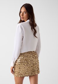 Witte blouse met kraag, gecombineerd met een gouden glinsterende minirok, voorzien van ronde pailletten in een gelaagd patroon, een gladde textuur en slim fit.