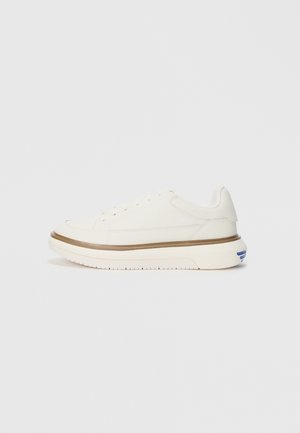 Weiße Leinensneaker mit niedrigem Profil, ausgestattet mit einer strukturierten Oberfläche, subtilen braunen Akzenten um die Sohle und blauen Details an der Ferse.