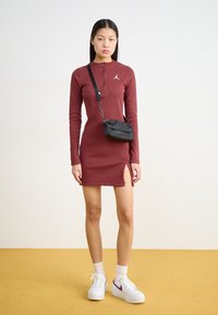 Abito lungo marsala a maniche lunghe con scollatura a zip e spacco laterale. Abbinato a sneakers bianche e a una piccola borsa a tracolla nera. Tessuto morbido.