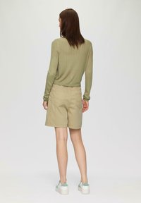 Hellgrünes, geripptes Langarmtop kombiniert mit beigen Shorts. Die Shorts haben Gesäßtaschen, und das Model trägt weiße Sneakers mit Minzakzenten.