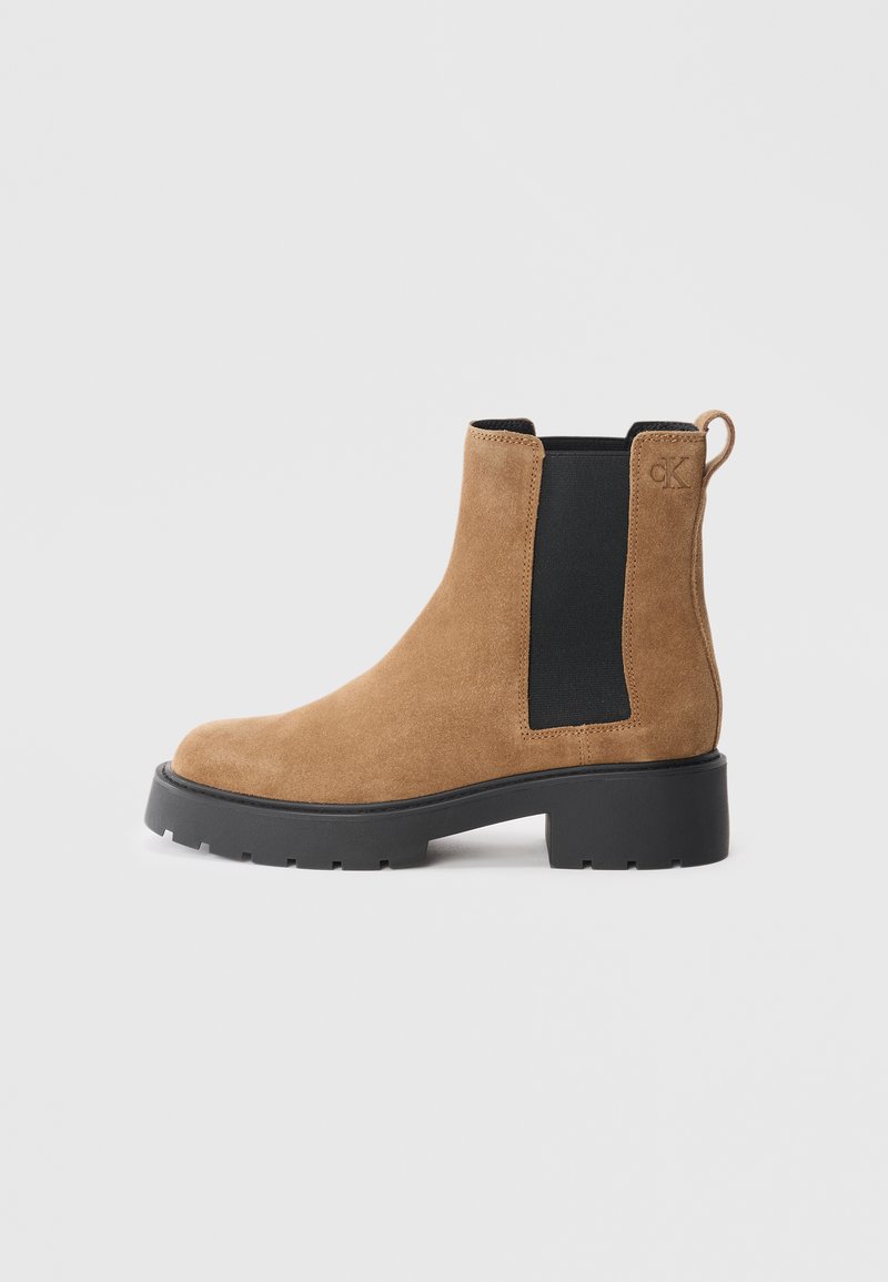 Tan suede Chelsea boot with black elastic side panels, rounded toe, and a chunky black rubber sole. Pull tab at the rear for easy wear.