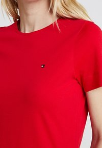 Czerwona bawełniana koszulka z okrągłym dekoltem, krótkimi rękawami oraz małym, markowym emblematem na lewej piersi. Gładka tekstura.