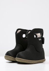 Botas de tobillo impermeables negras con un interior suave e insulated, puntera redonda y suela de goma. Presenta un cierre de botón y asas recortadas.
