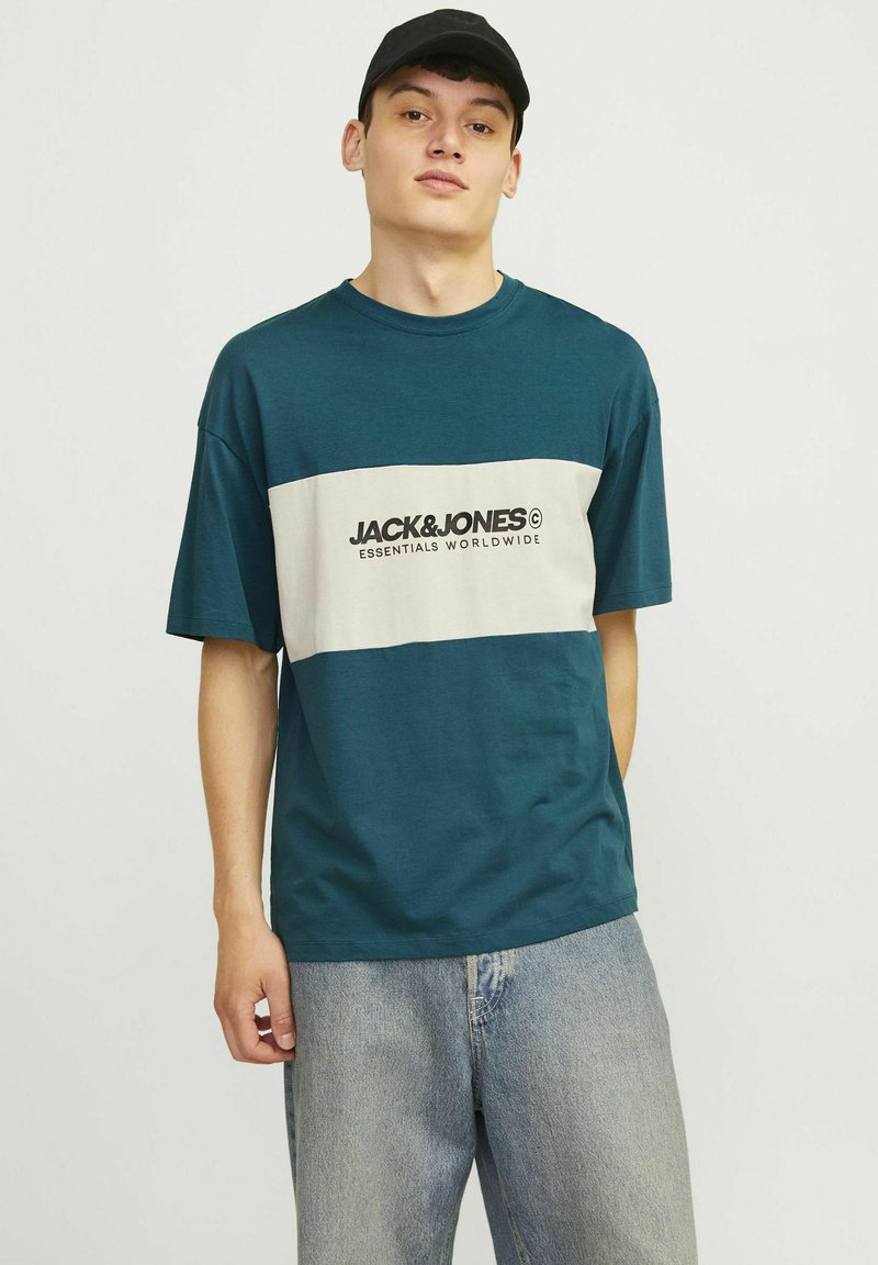 Teal crew-neck t-shirt med en cremefarvet vandret stribe og sort "JACK & JONES" logo. Løs pasform, lavet af bomuldsstof, parret med lyse denim jeans.