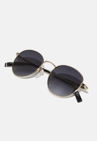 Round sunglasses with a gold metal frame, dark tinted lenses, and black temple arms featuring red and white stripes. Clear nose pads included.