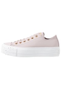 Zapatilla de color rosa claro con parte superior de piel suave, ojales dorados, suela de goma blanca y detalle de puntera moteada. Diseño de cordones de perfil bajo.