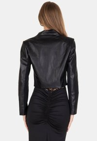 Giacca corta in pelle nera con una trama liscia, design su misura e maniche lunghe. Sul retro presenta un dettaglio in pizzo sotto l'orlo.