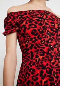 Röd leopardmönstrad klänning med avaxlad design, korta volangärmar, svarta knappar och en figurnära överdel. Mjuk tygtextur.
