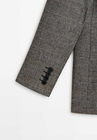 Manica di blazer grigio con motivo a quadri testurizzato, con tre bottoni neri al polsino e strisce contrastanti chiare e scure.