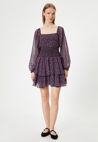 Vestido con escote cuadrado, largas mangas abullonadas y un corsé fruncido, con un fondo negro y un pequeño estampado de flores coloridas.