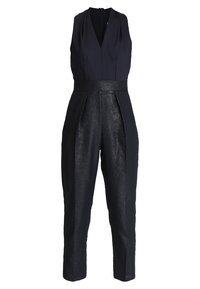Námořnický overal bez rukávů s hlubokým dekoltem a kontrastním lesklým černým pasem. Má tapered nohavice a skryté boční kapsy.