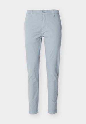 Hellblaue, schlanke Hose mit Gürtelschlaufen und Frontknopf, auf weißem Hintergrund dargestellt.