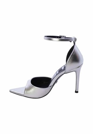 Sandalo argento con tacco alto, punta appuntita, fibbia alla caviglia, lati aperti e tacco a stiletto su sfondo bianco.