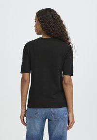 Haut court à manches courtes noir en maille, avec un col rond, présentant une texture lisse et une silhouette ajustée, associé à un jean bleu clair à jambes droites.