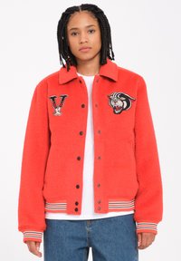 Veste polaire rouge avec une fermeture à bouton-pression noir, ornée d'un logo V brodé et d'un design de tigre sur la poitrine, et des poignets en rib dans des rayures.