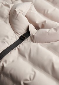 Lichtroze gewatteerd jack met een hoge kraag, een zwarte ritssluiting en een klein logolabel. De stof heeft een gladde, licht gestructureerde afwerking.