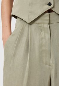 Ljus olivgrön cropped vest topp med V-ringning och en enkel knappstängning, kombinerad med skräddarsydda höga byxor med veck och fickor.