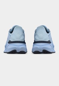 Ζευγάρι ανοιχτόχρωμων αθλητικών παπουτσιών, εμφανιζόμενα από την πίσω πλευρά, με υφή στον σχεδιασμό της φτέρνας και μαύρα διακοσμητικά στη σόλα, πάνω σε λευκό φόντο.