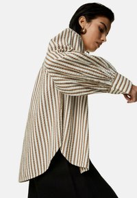 Gestreepte blouse in beige en bruine stof, met een relaxte pasvorm, poffende mouwen, knoopmanchetten en een afgeronde zoom voor extra detail.