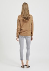 Brun stickad tröja med ribbad fåll, matchad med ljusgrå tajta jeans och svarta öppna klackskor. Fokusera på färg och textur.