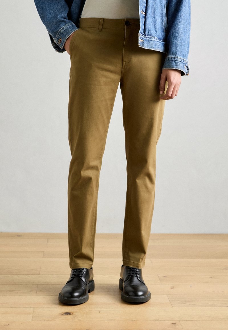 Tana chinos van glad katoen, met een slim fit en zijzakken, gecombineerd met zwarte leren schoenen.